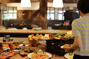 Person am Frühstücksbuffet mit Obst, Käse, Lachs und Joghurt in gemütlich eingerichteter Gaststube.