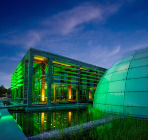 Grün beleuchteter Dänischer Pavillon mit moderner Glasfassade und Kuppel bei Abenddämmerung.