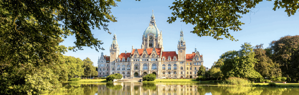 Neues Rathaus Hannover, frontal aufgenommen bei Sonnenschein, gespiegelt im davorliegenden Teich.