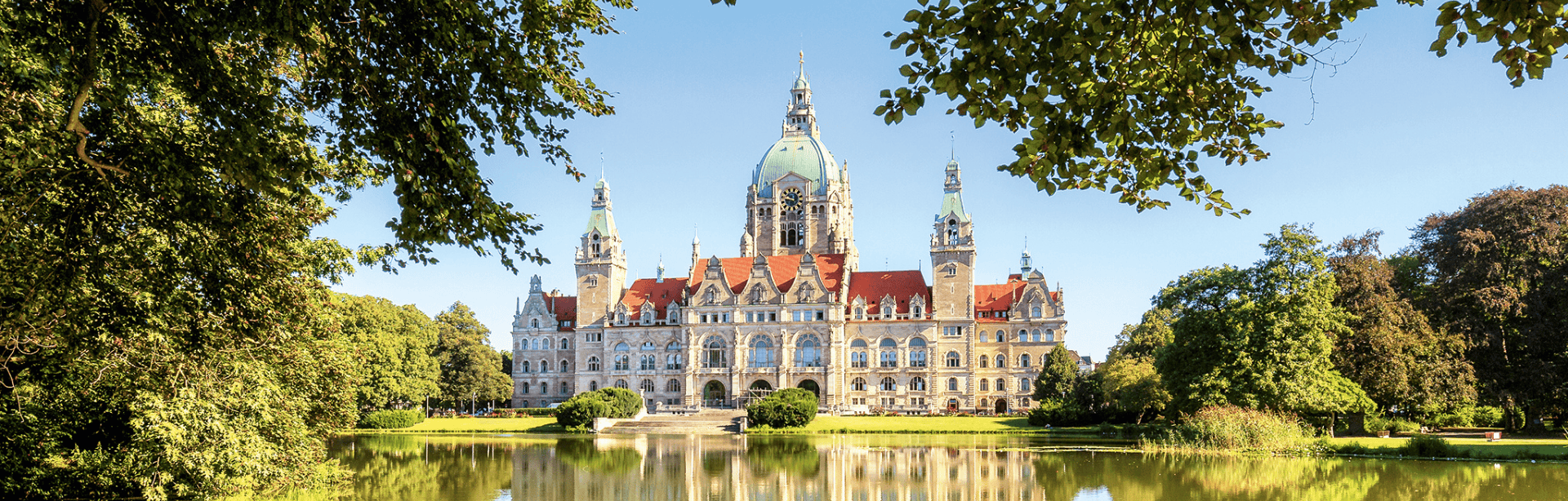 Neues Rathaus Hannover, frontal aufgenommen bei Sonnenschein, gespiegelt im davorliegenden Teich.