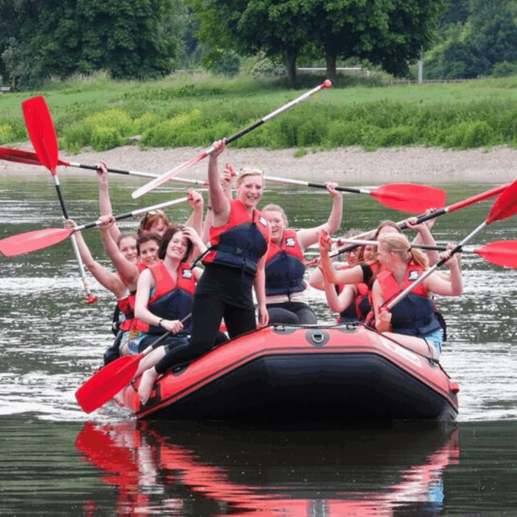 Gruppe junger Frauen beim fröhlichen Paddeln in einem Schlauchboot auf einem ruhigen Fluss.