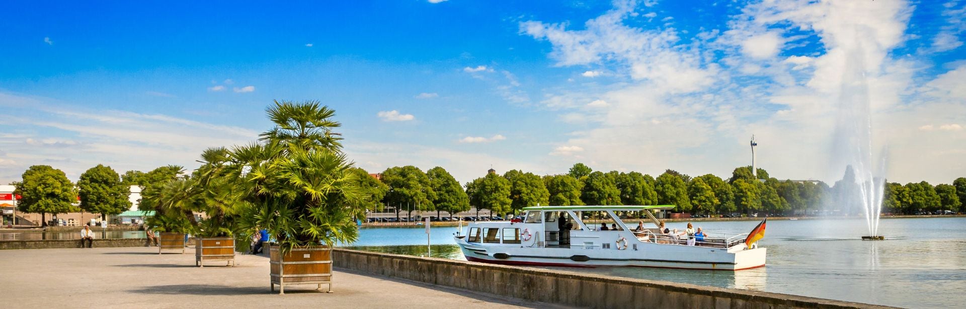 Weiße Ausflugsfähre auf dem Maschsee in Hannover, rechts ein hoher Wasserfontänenbrunnen.